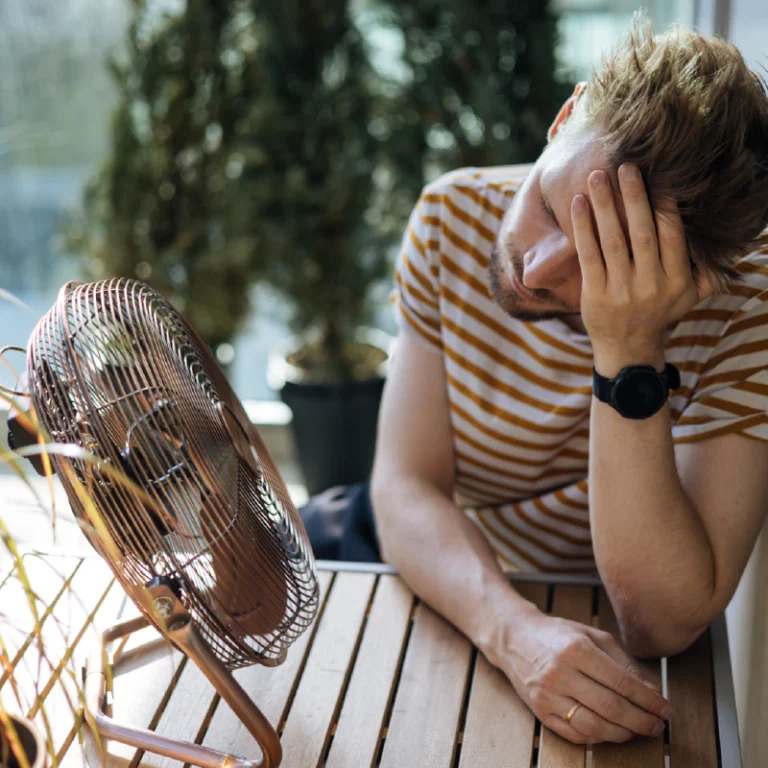 un homme devant un ventilateur épuisé par la chaleur